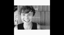 a young man in a black tank top is smiling in a black and white photo .