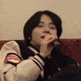a young man is sitting on a couch holding a microphone to his mouth .