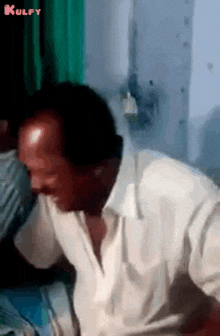 a man in a white shirt is sitting on a bed with his head down .
