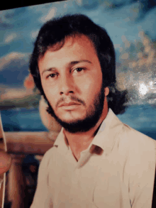 a man with a beard wearing a white shirt looks at the camera
