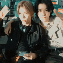 two young men sitting next to each other one wearing headphones and the other wearing a black jacket with the word armani on it