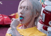 a man in a yellow shirt is eating a blue gummy bear