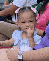 a little girl with a pink bow in her hair is eating a piece of food