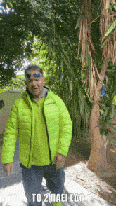 a man wearing sunglasses and a givova jacket stands in front of a palm tree