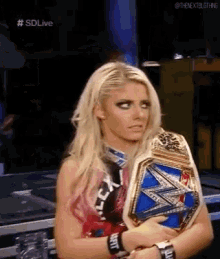 a woman is holding a wrestling championship belt and looking at the camera .