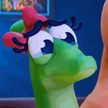 a close up of a green cartoon character with a red bow on its head