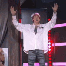 a man with pink hair is standing on stage with his arms in the air