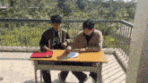 two boys are sitting at a desk with one wearing a jacket that says icon