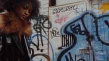 a woman standing in front of a wall that has graffiti on it including the word say