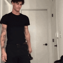 a man in a black shirt and black shorts is standing in front of a door .