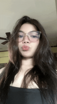 a woman wearing glasses and a black tank top is taking a selfie in front of a ceiling fan .
