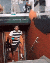 a man in a striped shirt is walking through a doorway that says " deration francaise de tennis " on it