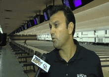 a man wearing a shirt that says rsp is talking into a microphone in a bowling alley