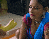 a woman in a blue and pink blouse holds a banana
