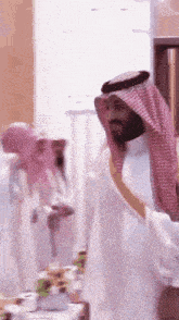 a man in a saudi arabian costume is standing in front of a table with food .