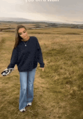 a woman wearing a blue sweater and jeans is walking in a field