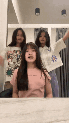 three girls are posing for a picture in front of a mirror .