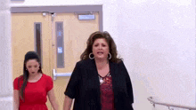 two women are walking down a hallway holding hands .