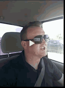 a man wearing sunglasses and a black shirt is driving a car