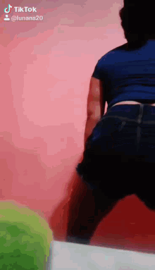 a woman in a blue shirt and shorts is dancing in front of a pink wall .