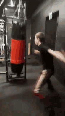 a young boy is jumping in front of a boxing bag in a gym .