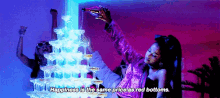 a woman is pouring a bottle of champagne into a pyramid of champagne glasses .