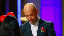a bald man in a suit is talking to a woman