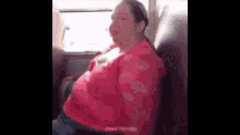a woman in a pink shirt is sitting on a bus with her breast exposed .