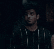 a man in a black and white striped shirt is standing in the dark with a hand reaching out towards him .