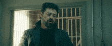 a man with a beard and a black coat is standing in front of a door .