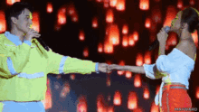 a man and a woman are holding hands while singing into microphones on a stage that says maywizard