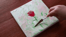 a person is painting a red rose on a green and white background