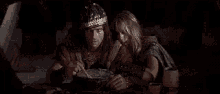 a man and a woman are sitting at a table eating food from a bowl .