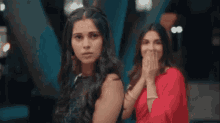two women are standing next to each other covering their mouths with their hands .
