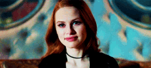 a woman with red hair and a choker is sitting on a couch and smiling .