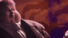 a fat man in a suit and tie is sitting in front of a balloon .