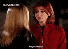 two women are standing next to each other and talking to each other . one of the women is wearing a red jacket .
