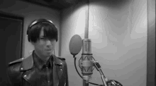 a man wearing headphones and a leather jacket is singing into a microphone in a recording studio .