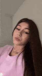 a young woman with long brown hair is wearing a pink shirt and a necklace .