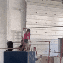 a girl in a red shirt stands on a bar in front of a garage door