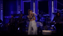 a woman is singing into a microphone on a stage with a band behind her