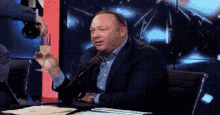 a man in a suit is sitting at a table with a microphone and a glass of wine .