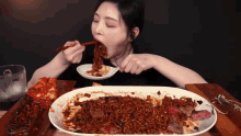 a woman is eating noodles with chopsticks and a spoon