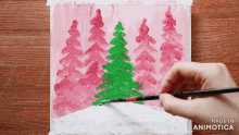 a person is painting a christmas scene with trees in pink and green