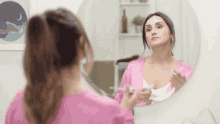 a woman in a pink robe is brushing her teeth in a bathroom mirror