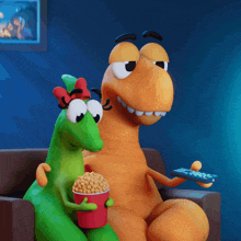 two cartoon dinosaurs are sitting on a couch eating popcorn and watching tv