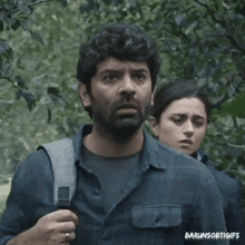 a man with a beard is standing next to a woman in a forest .