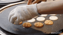 a person wearing a white glove is putting a cookie on a griddle