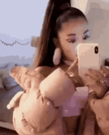 ariana grande is taking a selfie with her cell phone while sitting on a bed .
