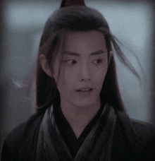 a man with long hair is wearing a black kimono and looking at the camera .